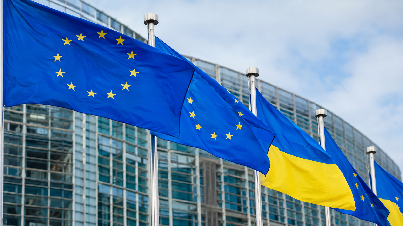 Знамена на Европейския съюз и Украйна пред модерна европейска институционална сграда на фона на нарастващо напрежение между Русия и Запада